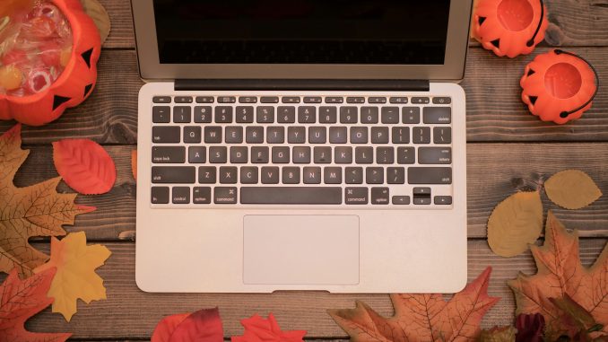 Halloween pumpkins with fallen leaves and laptop on the wooden background October remote jobs