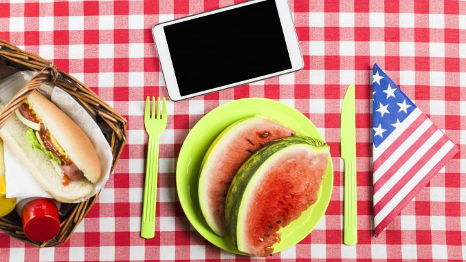 Memorial Day Remote Jobs - Virtual Vocations Telecommute Jobs Memorial Day Remote Jobs - Red and white checked table cloth over table with American flag napkin folded into a triangle and Memorial Day cookout food. A phone sits on the table above the plate of watermelon.